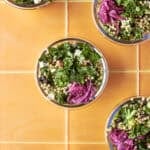 Overhead shot of salsa verde chopped salad meal prep bowls with kale, giant couscous, chicken and pickled red onion.