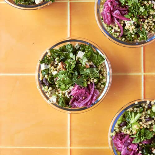 Overhead shot of salsa verde chopped salad meal prep bowls with kale, giant couscous, chicken and pickled red onion.