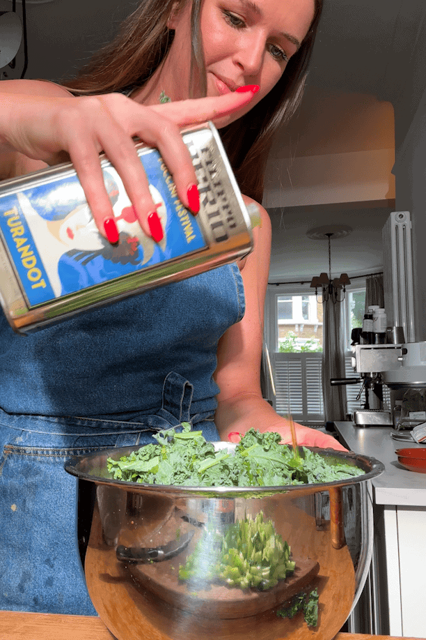 Salsa verde dressing being poured over kale in a large mixing bowl.