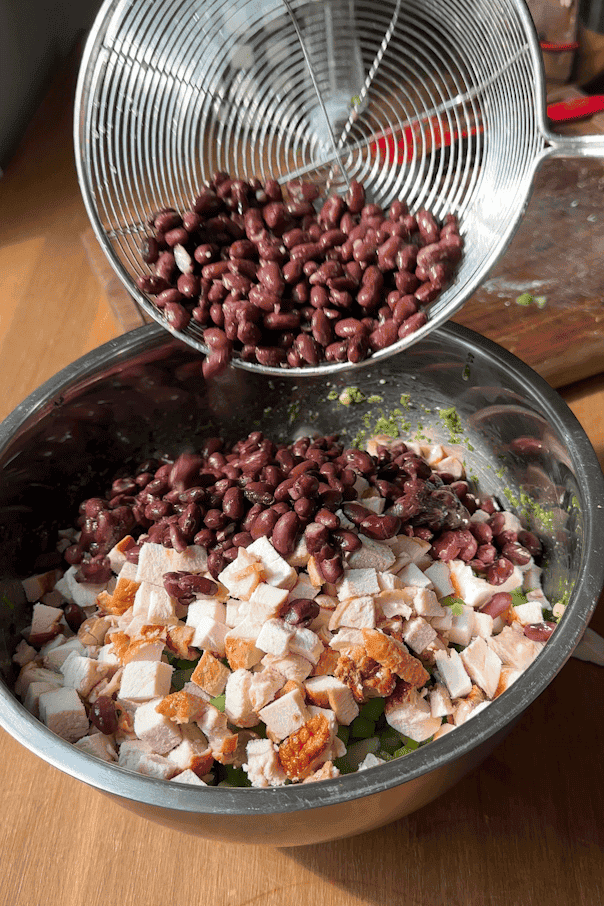 Black beans and chopped chicken breast being added to the salad bowl.