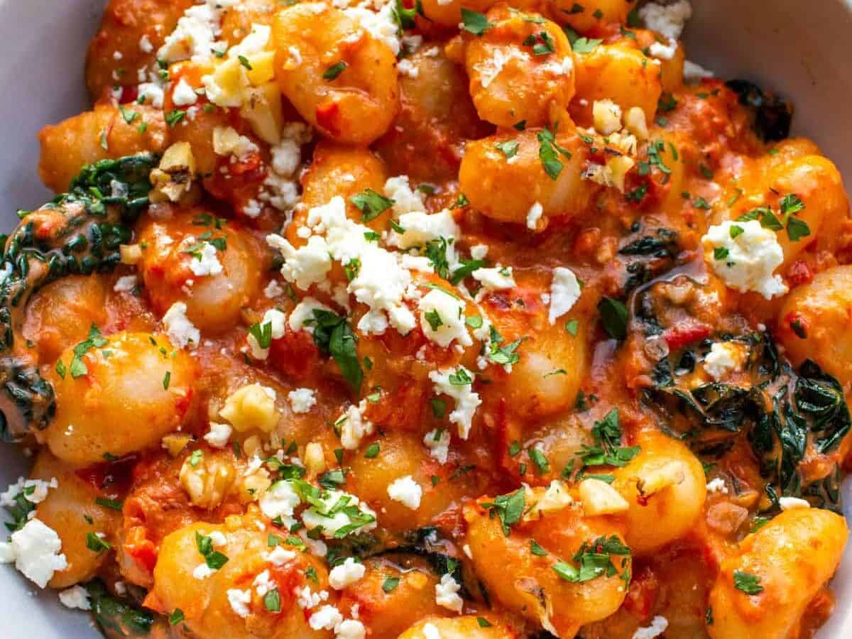 Bowl of gnocchi in tomato sauce with wilted spinach, topped with crumbled feta cheese and chopped parsley.