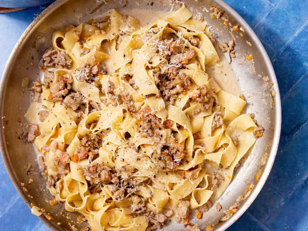 Creamy ragu bianco tossed with fresh pappardelle and topped with grated parmesan and black pepper in a stainless steel pan.