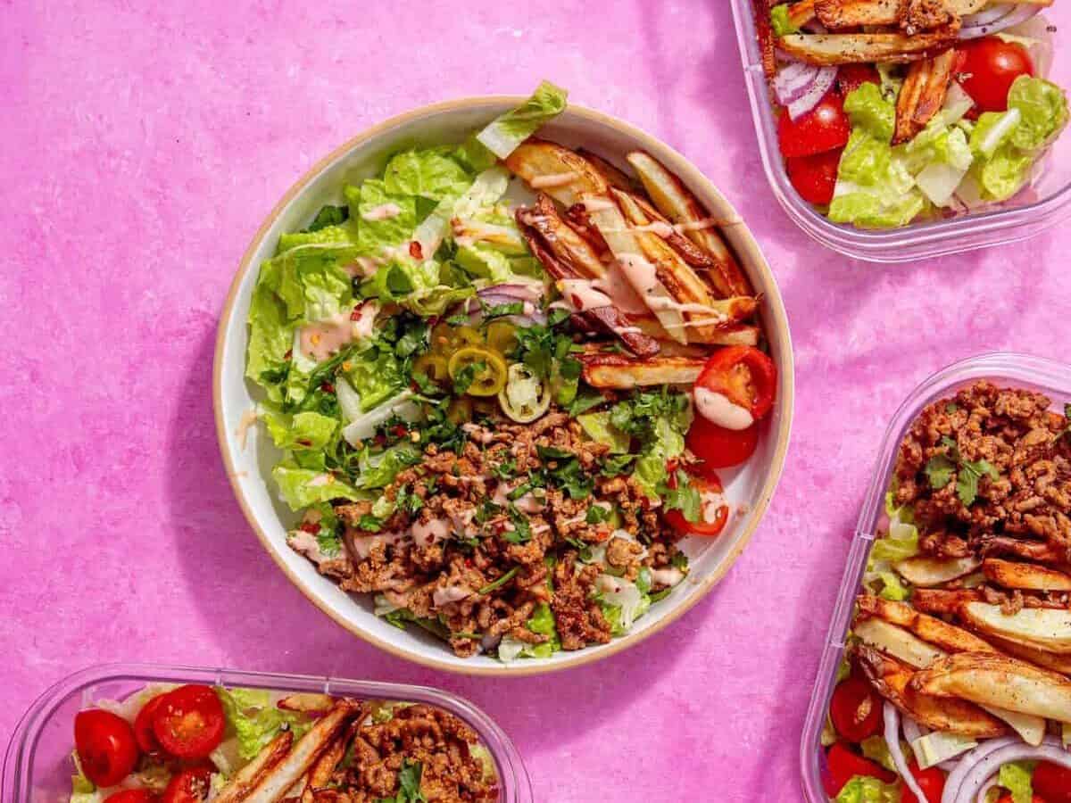 image of prepared burger bowl with other meal prep bowls around it on a pink background