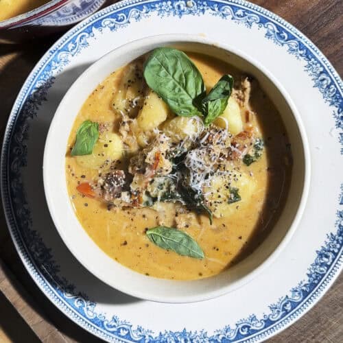 Bowl of creamy tuscan gnocchi soup with crispy sausage, kale, sundried tomatoes, parmesan and fresh basil.