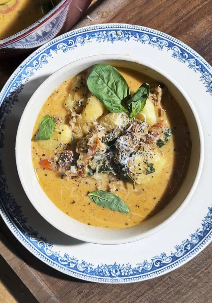 Bowl of creamy tuscan gnocchi soup with crispy sausage, kale, sundried tomatoes, parmesan and fresh basil.