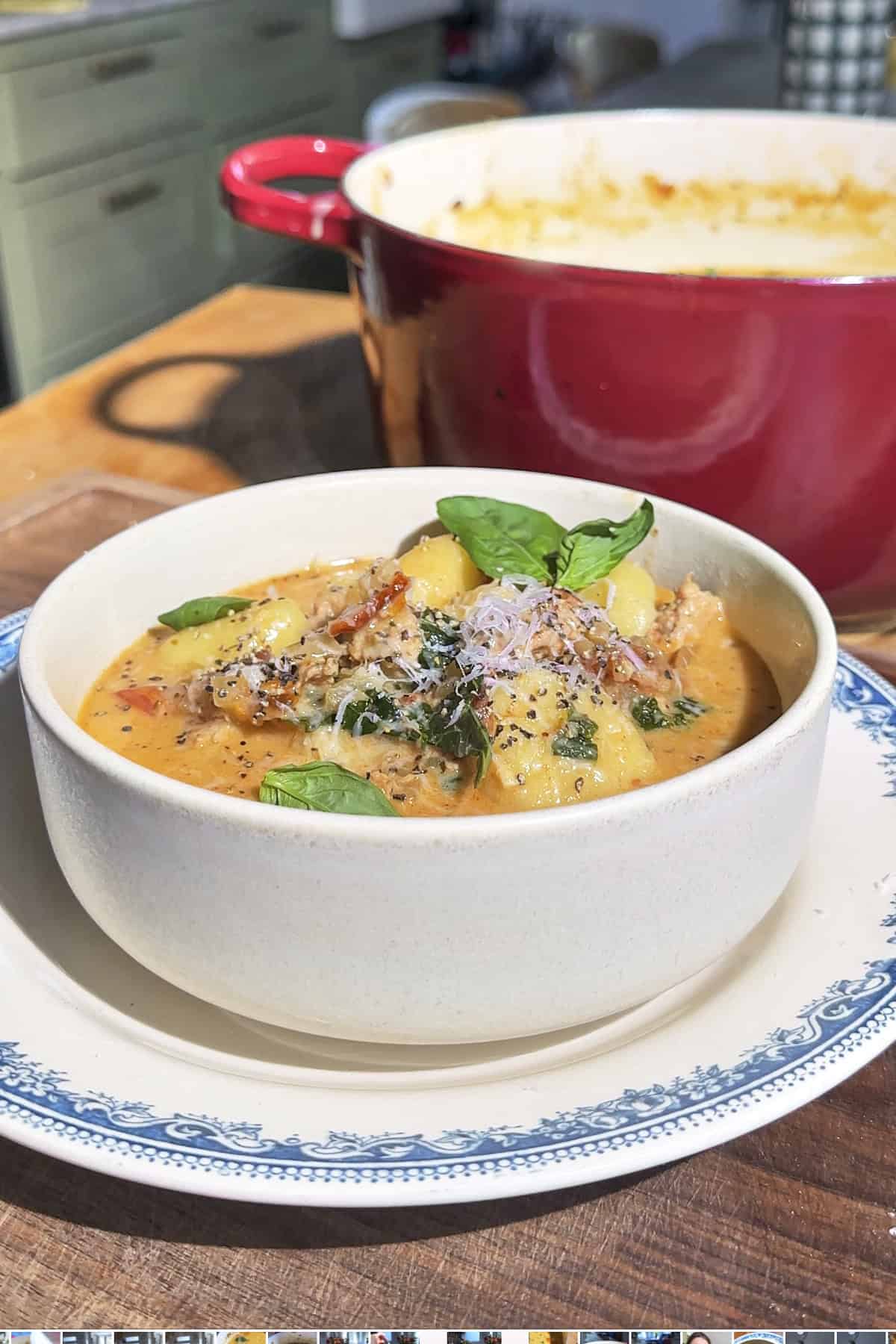 Close-up of creamy tuscan gnocchi soup topped with grated parmesan, basil and black pepper.