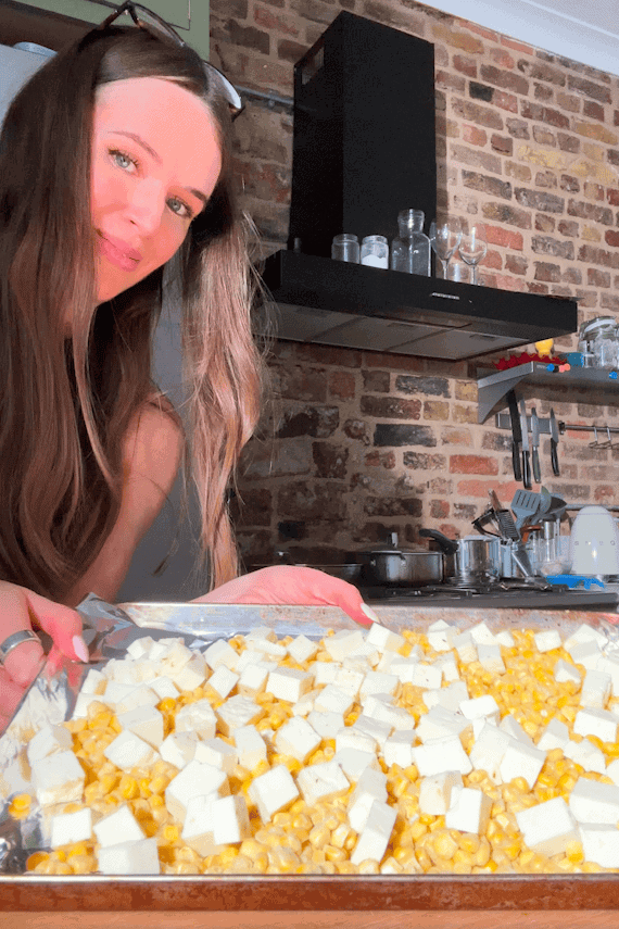 Cubed halloumi and frozen sweetcorn roasting on a lined baking tray.
