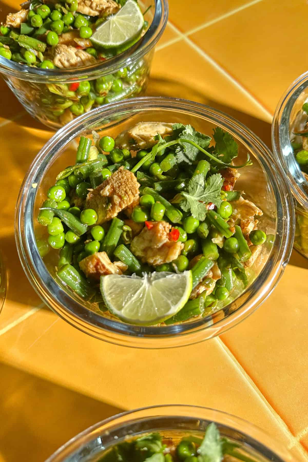 Close-up of chicken pea salad with green beans, coriander and a wedge of lime in a glass container.