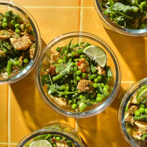 Meal prep containers of chicken pea salad with green beans, shredded chicken and lime wedges.