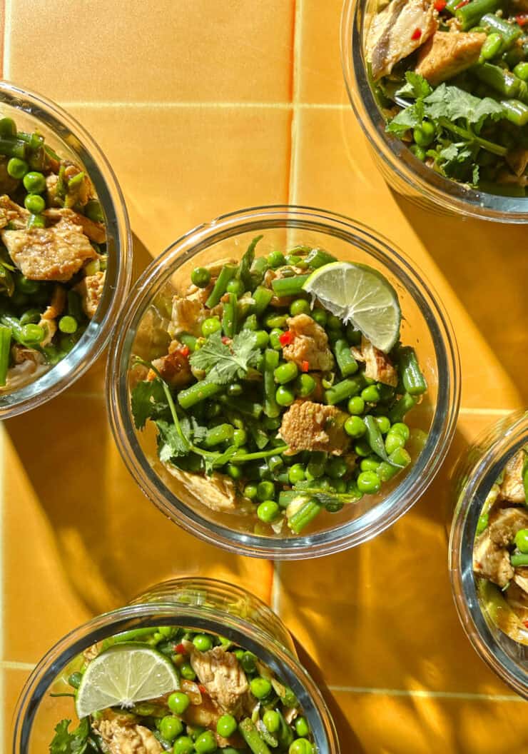 Meal prep containers of chicken pea salad with green beans, shredded chicken and lime wedges.