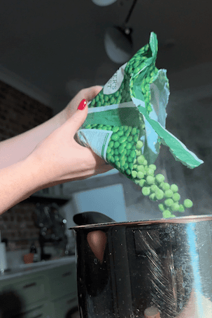 Frozen peas being poured from the bag into the pan.