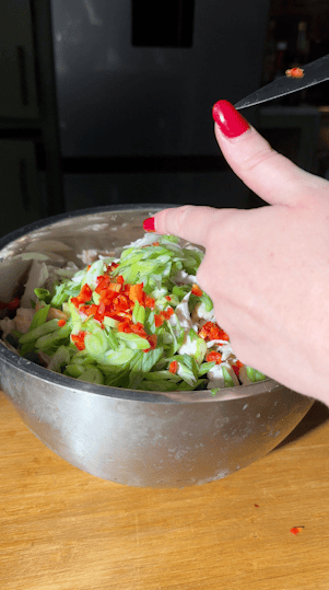 Sliced spring onions and chopped chilli added to shredded chicken in a large bowl.