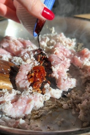 Hot honey being drizzled over raw chicken mince in a frying pan.