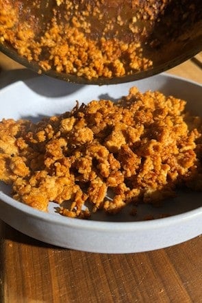 Golden, sticky cooked chicken mince being tipped from a pan into a white bowl.
