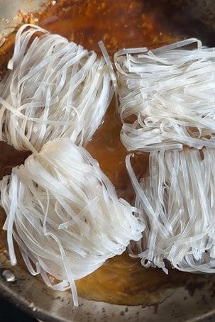 Nests of dried rice noodles soaking in water.